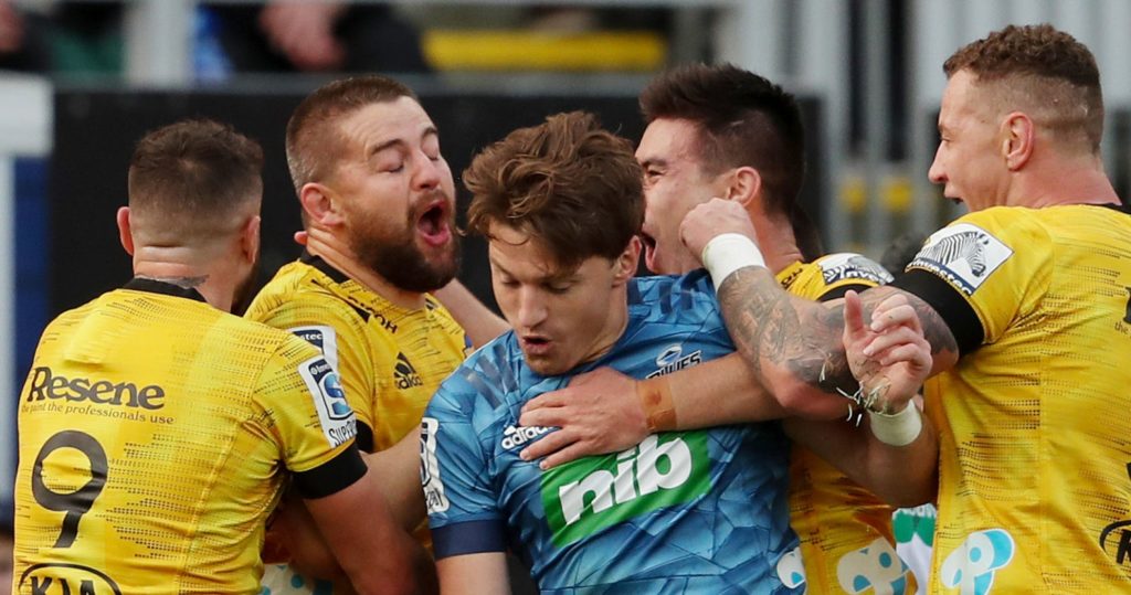 The Hurricanes' players celebrate a try as Blues' Beauden Barrett (C) is caught in the middle during the Super Rugby match between the Auckland Blues and Wellington Hurricanes at Eden Park stadium in Auckland on June 14, 2020. (Photo by MICHAEL BRADLEY / AFP) (Photo by MICHAEL BRADLEY/AFP via Getty Images)