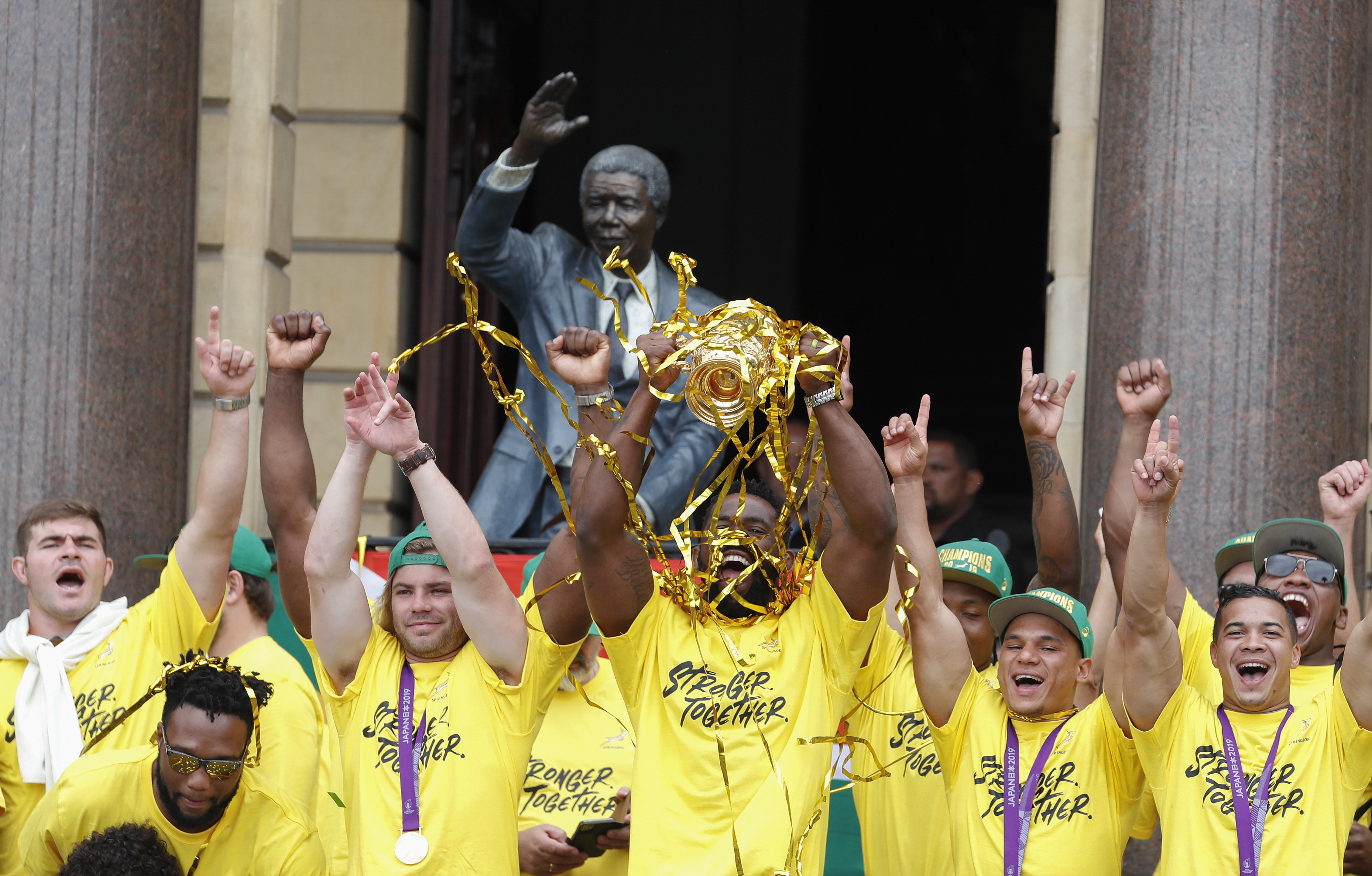epa07988127 South African rugby captain Siya Kolisi (C) holds up the Webb Ellis Cup with his team in front of a bust of former president Nelson Mandela at the Cape Town City Hall during a trophy tour in Cape Town, South Africa 11 November 2019. Tens of thousands of South Africans came out to see the Springboks finish their nation wide trophy tour in Cape Town after winning the Rugby World Cup. South Africa won the Webb Ellis Cup after defeating England 32-12 in the Rugby World Cup final played in Japan on 02 November 2019. EPA/NIC BOTHMA